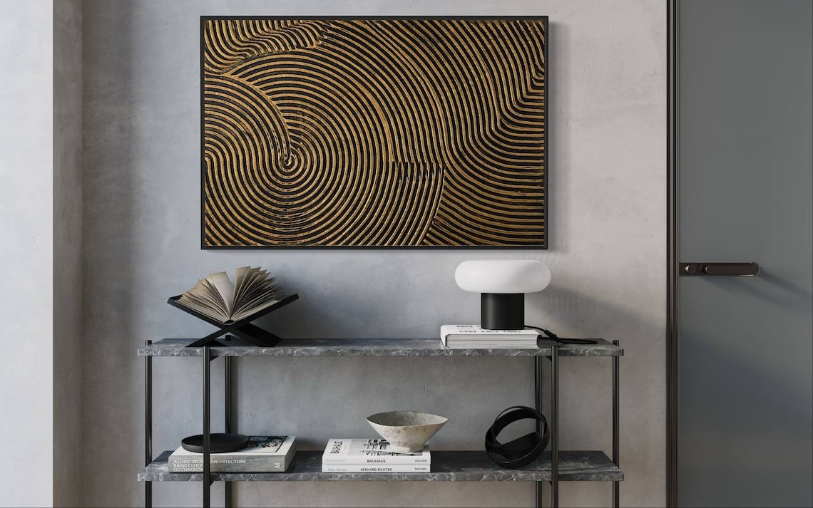 Metallic abstract canvas painting with gold and black concentric circular patterns.